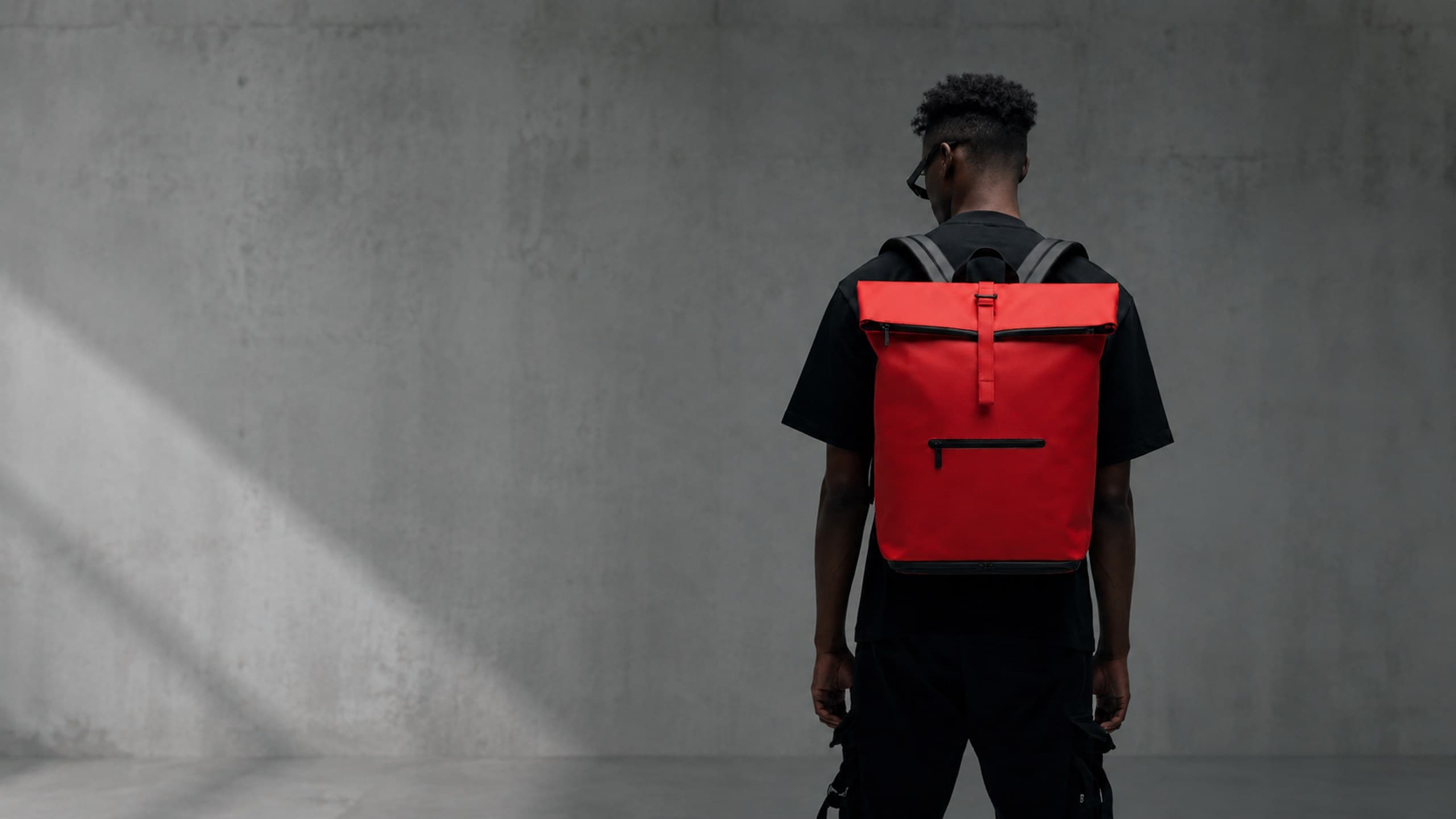Model wearing NORJ red backpack against concrete wall